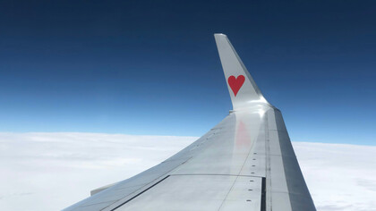 A plane's wing with a heart logo, soaring above the clouds