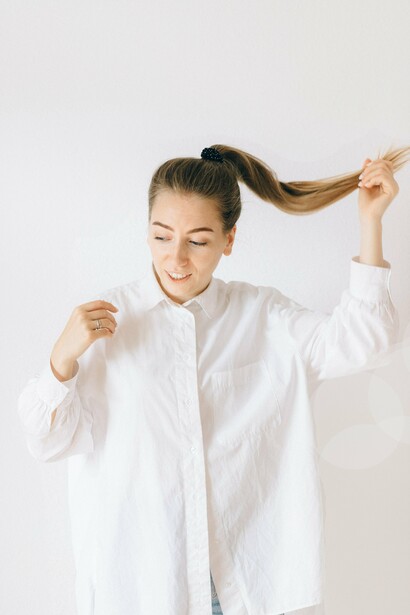 A woman wearing a white shirt holding her hair