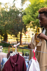 A man sifts through second-hand clothes at a yard sale, making mindful choices to resist the lure of fast fashion and support a more sustainable, circular economy