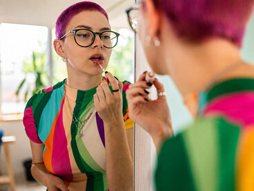 Young woman with dyed pink hair applying makeup in front of a mirror
