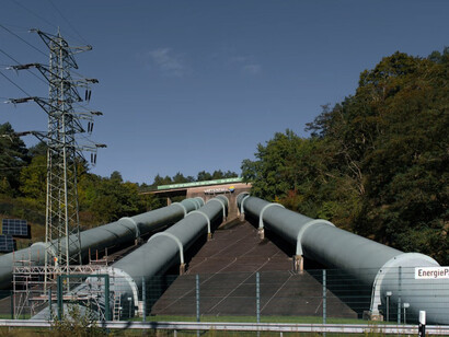 A large pipe stands next to a forest in Geesthacht, Germany, where summer energy, electricity, and vibrant trees coexist harmoniously