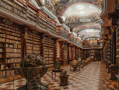 Rows of antique books surrounded by globes and elaborate Baroque decoration, reflecting the meeting of scholarship, science, and beauty within the Klementinum, Prague