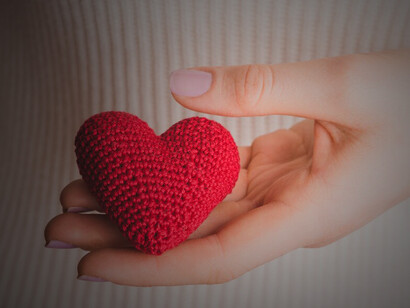 Close-up of hands gently clasping a knitted heart, representing affection and connection