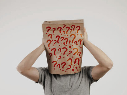 A person with a paper bag over their head, marked with question marks, symbolizing confusion or mystery