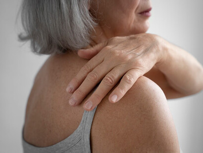 An elderly woman showing signs of joint discomfort while standing in a calm pose