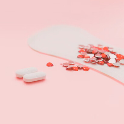 Una toalla sanitaria llena de lentejuelas y dos píldoras antiinflamatorias