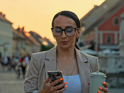 Businesswoman enjoying a coffee while using her smartphone during a walk through Ljubljana’s city streets