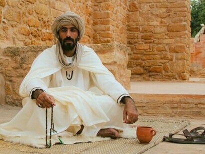 A man seated in flowing white traditional clothing and a wrapped head covering, symbolising heritage, spirituality, and cultural continuity