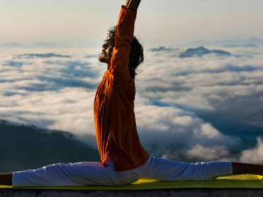 A man practicing yoga on a building edge, framed by the open sky and natural light
