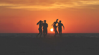 Dos parejas bailando en la playa frente al atardecer