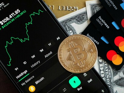 A Bitcoin trading interface surrounded by payment cards and cash, symbolising the rapid evolution of digital financial ecosystems