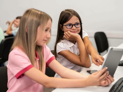 Due bambine, sedute a un banco in un'aula scolastica, stanno lavorando insieme su un tablet
