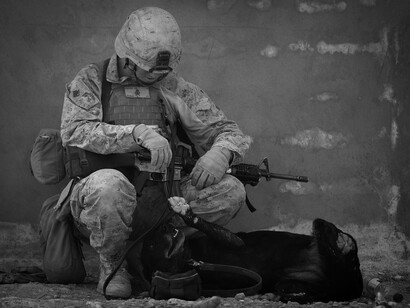 A military man sits, armed with a weapon in his hands