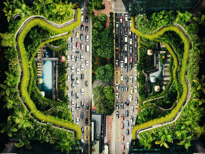 A busy road is surrounded by green spaces in surrounding buildings