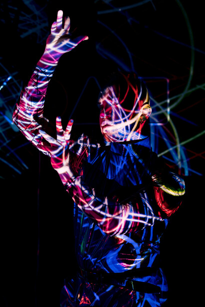 A man stands in a dark room lit by soft string lights, lightning flickering through his body like an inner storm