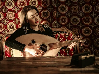 A woman striking the strings of an oud with quiet grace, representing the intimate connection between music and memory