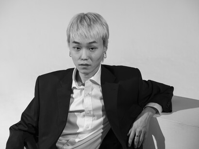 A minimalist black-and-white portrait of a young man posing in front of an empty backdrop, capturing a quiet and contemplative atmosphere