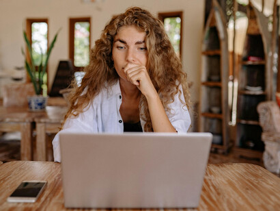 A woman in a white button-up shirt uses a laptop, her expression reflecting visible frustration