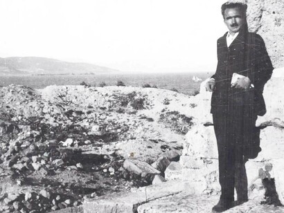 Nikos Kazantzakis leaning against a stone wall in the countryside of Greece