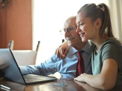 A grandfather and granddaughter using a laptop together 