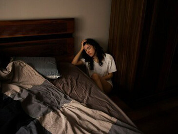 A young woman experiencing anxiety, sitting on the floor near her bed