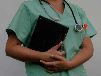 A stethoscope hangs around the neck of a medical professional wearing a green uniform