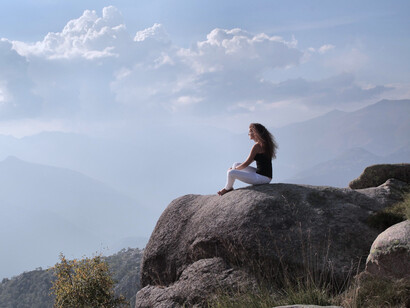 A woman resting on a rock overlooking distant peaks, reflecting the calm that emerges when the mind and body work in harmony