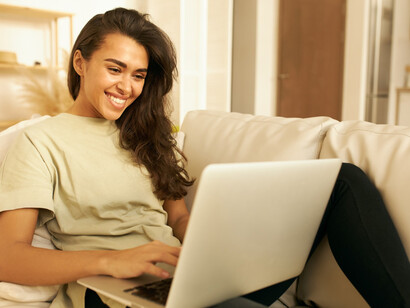 A young woman waves at her computer screen during a virtual AI therapy session, highlighting the growing intersection of technology and mental health care