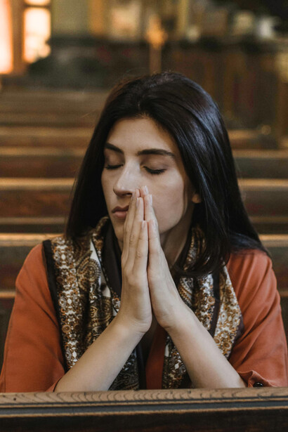 A brunette woman kneels in a church as she prays