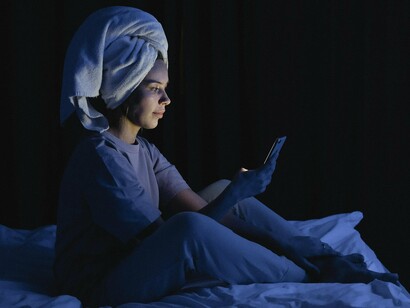 A woman illuminated by her phone screen in a dark bedroom, representing the cognitive overstimulation that lingers beyond scrolling
