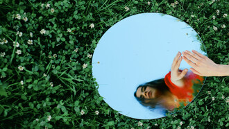 Amidst a lush green field, she gazes intently at her reflection, reminding us that in storytelling, true emotional depth comes from embracing vulnerability
