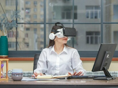 A young lady sitting at a desk, wearing VR glasses, and looking to the side