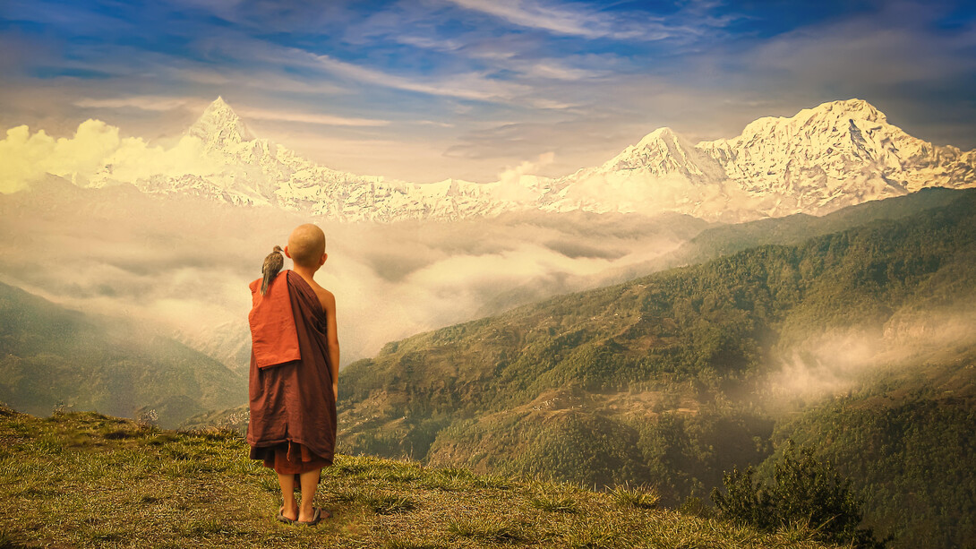 A young Buddhist monk standing on the mountains in nature, with a bird on his shoulder