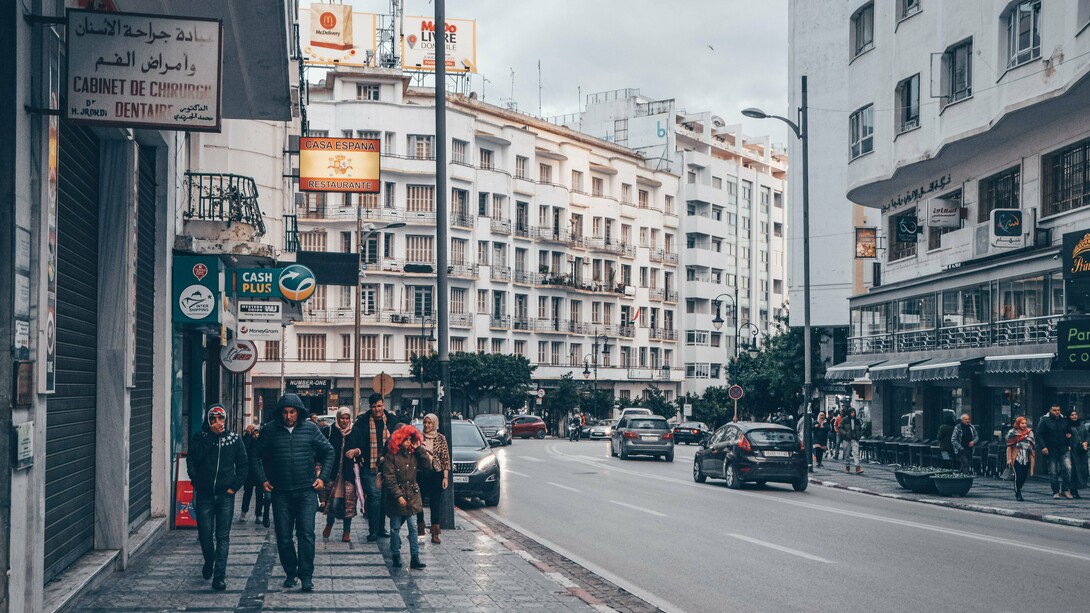 Pedestrians moving through a commercial district surrounded by Moroccan and international businesses in Tangier, Morocco, representing the diverse communities shaped by migration and mobility