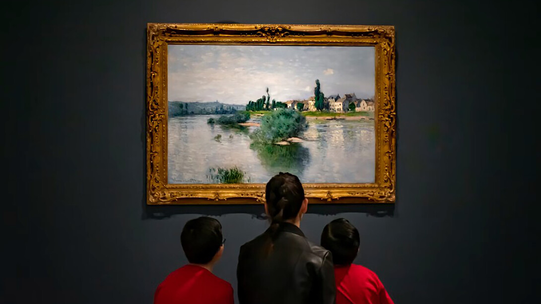 A woman in a black jacket sits on a red sofa with two children inside an art museum