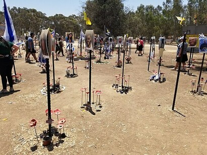 Des visiteurs, civils et soldats, se recueillent devant les portraits des victimes du festival Nova, érigés dans le désert du Néguev en Israël, sur fond de drapeaux israéliens flottant au vent