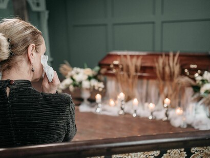 A grieving woman stands beside a flower-adorned coffin during a funeral service