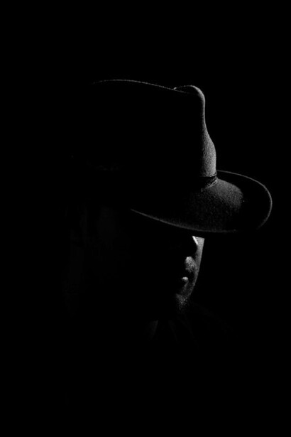 Dressed in a black suit and white fedora, the man carries the unmistakable presence of a seasoned criminal