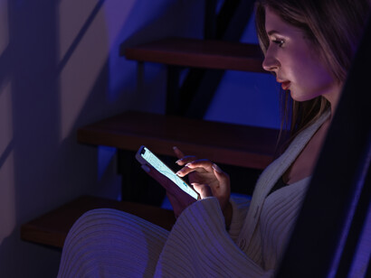 A young woman sits on the stairs at night, her face lit by her phone, capturing the quiet grip of digital addiction
