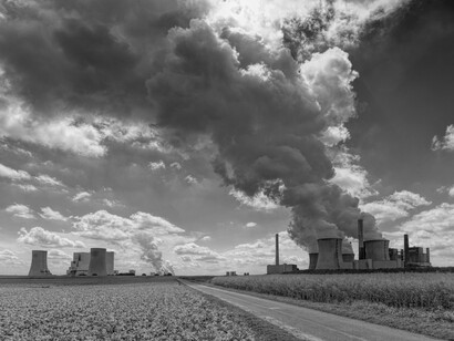 The towering smokestacks represent the ongoing fossil energy production that continues to exacerbate global climate disruption