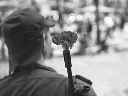 Revolução dos Cravos em Portugal. Ao apontar o céu, gritar e pular, Nuno fez um sinal a chamar Maria para perto de si. Contagiados pelas cores que a refração e reflexão da luz solar em gotículas de água fazem, não conseguiram parar de sorrir e vibrar
