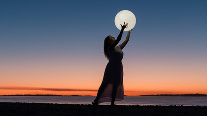 Mulher brinca com projeção com uma lua inflável no atardecer na praia