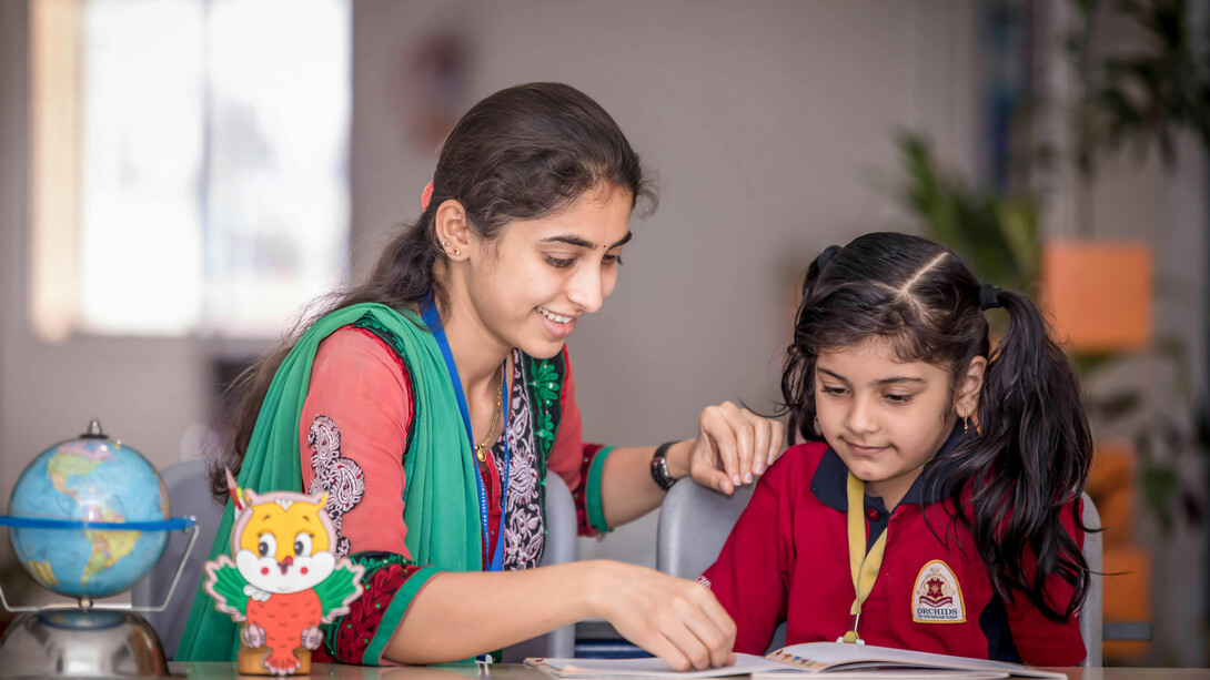 Uma professora auxilia uma aluna em seus estudos, demonstrando a importância do suporte individualizado no processo de aprendizagem