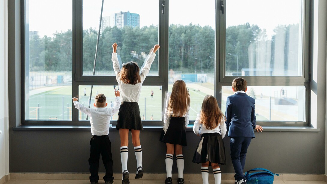 Students in school uniforms seen from behind, looking outside