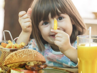 A young girl enjoys ultra-processed fast food at a cafe, highlighting the prevalence of unhealthy junk food for children