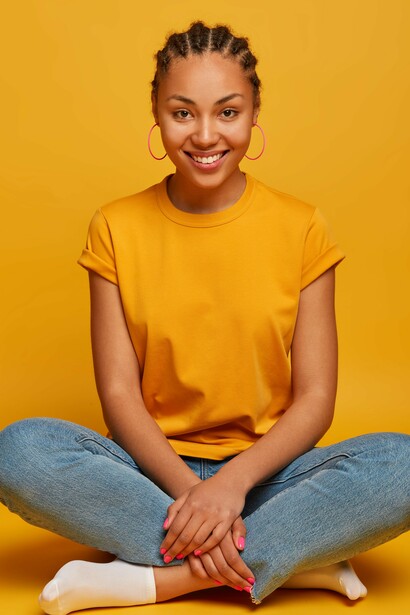 A woman sitting cross-legged on the floor, looking joyful, peaceful, and relaxed