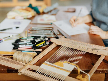 A close-up of an anonymous craftswoman's hand drawing near a manual weaving loom machine