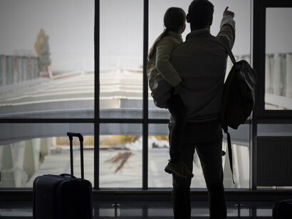 A man and his child await their flight at the airport, embarking on a journey abroad for new opportunities