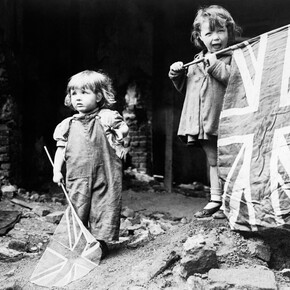 Two small girls waving their flags to celebrate the end of the war in the rubble of Battersea on VE Day