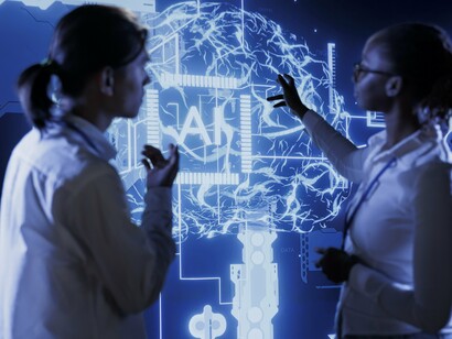 Two professionals stand before a glowing digital brain interface, symbolizing how AI demands both collaboration and critical thinking to be used effectively